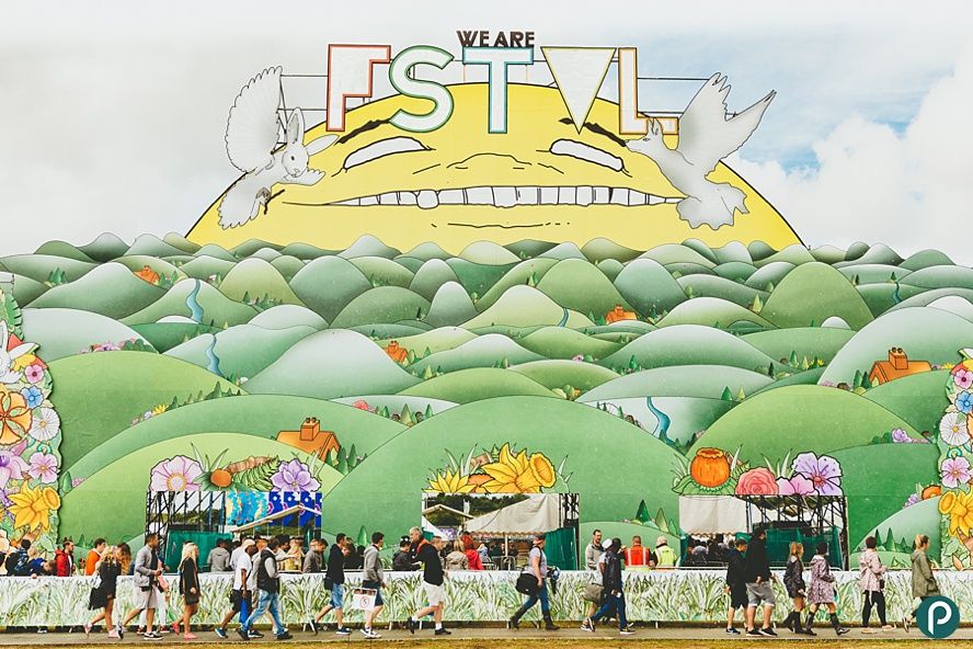 The entrance to We Are Fstvl with a large wall with drawn on trees and people walking in front