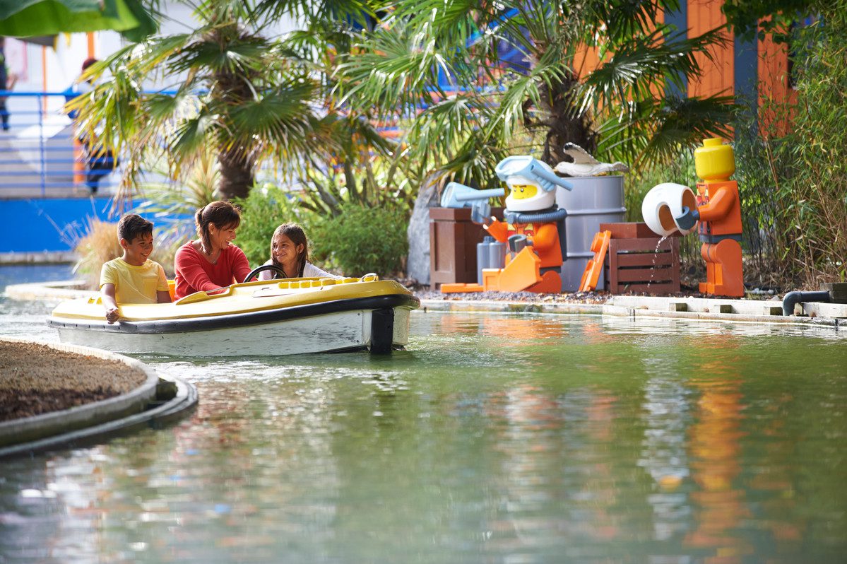A water LEGO themed ride area with a yellow boat with 3 people inside