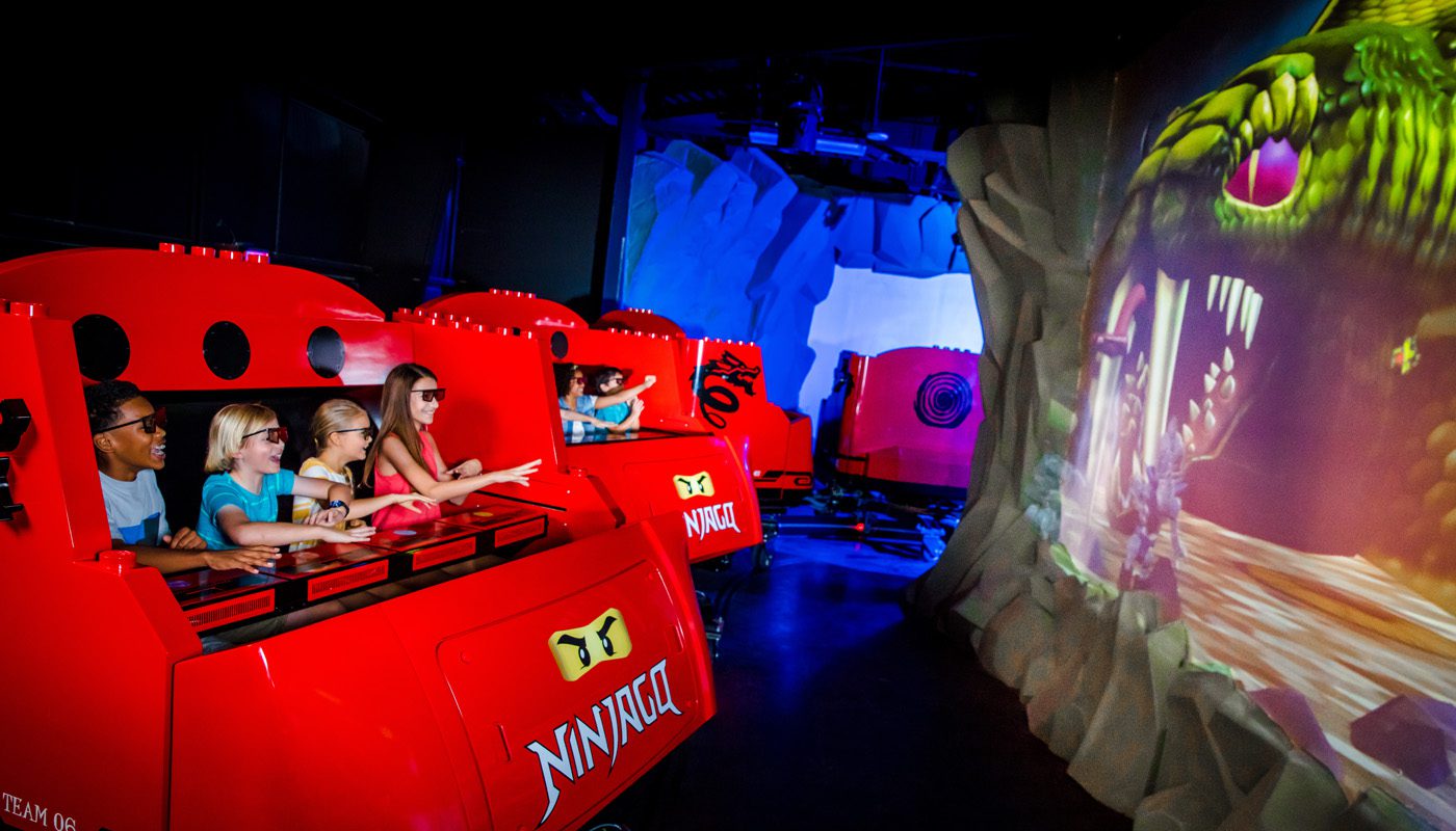 Inside of a LEGO Ninjago themed ride with people in red carriages while wearing glasses