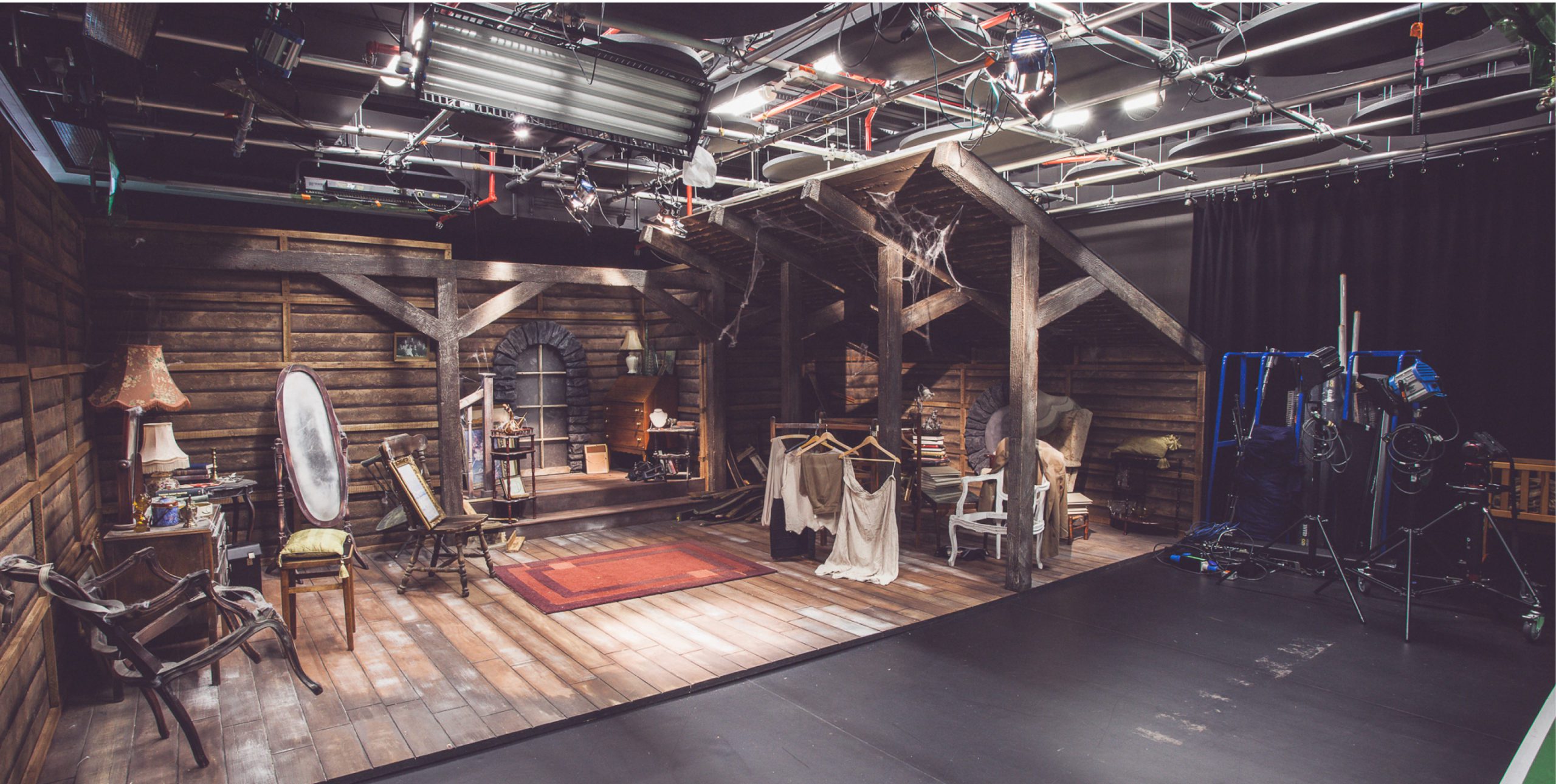 A set on a stage for a room that includes chairs, a mirror, a carpet and clothing
