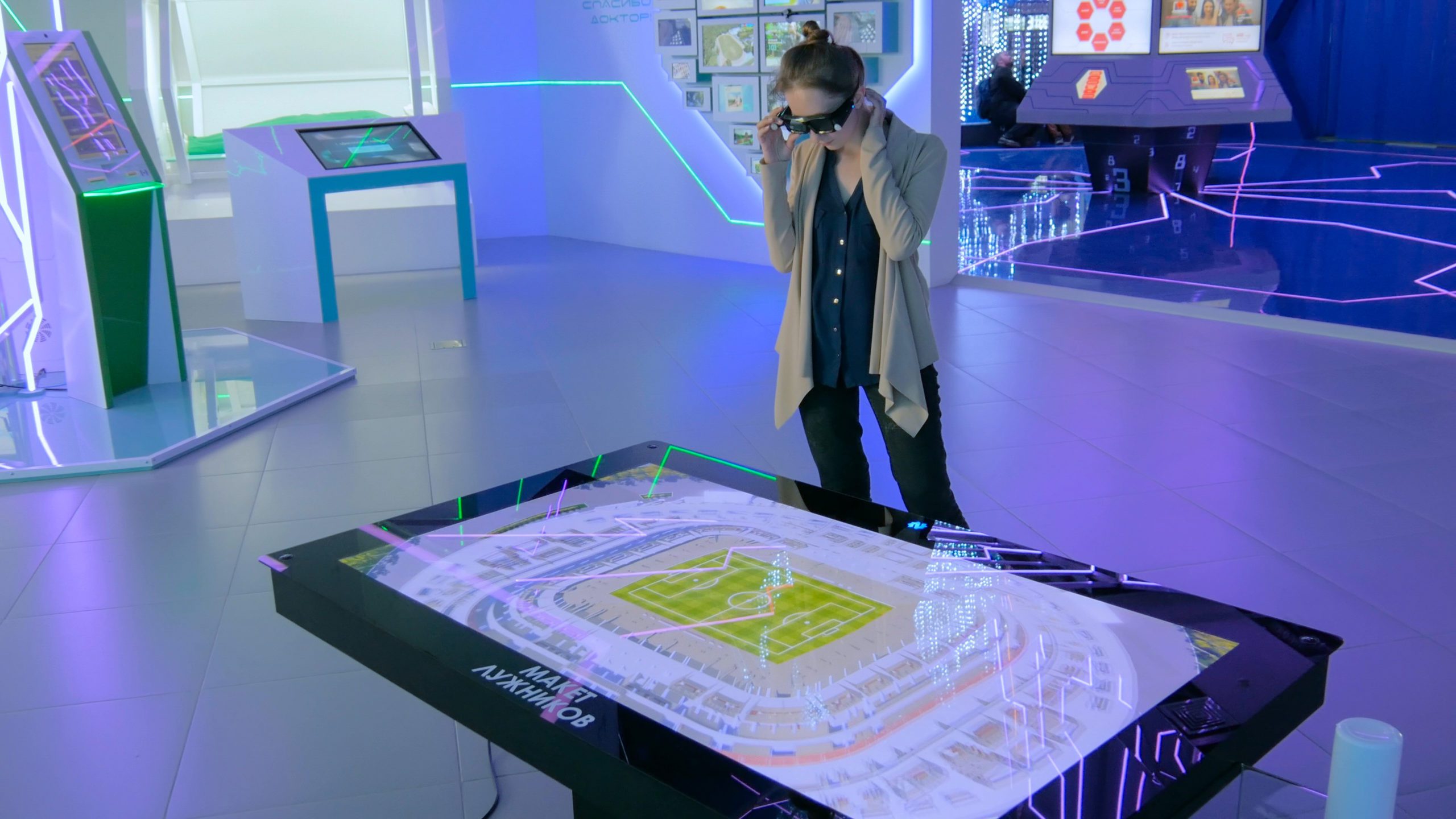 A building with a person inside looking a football pitch on a screen while wearing glasses