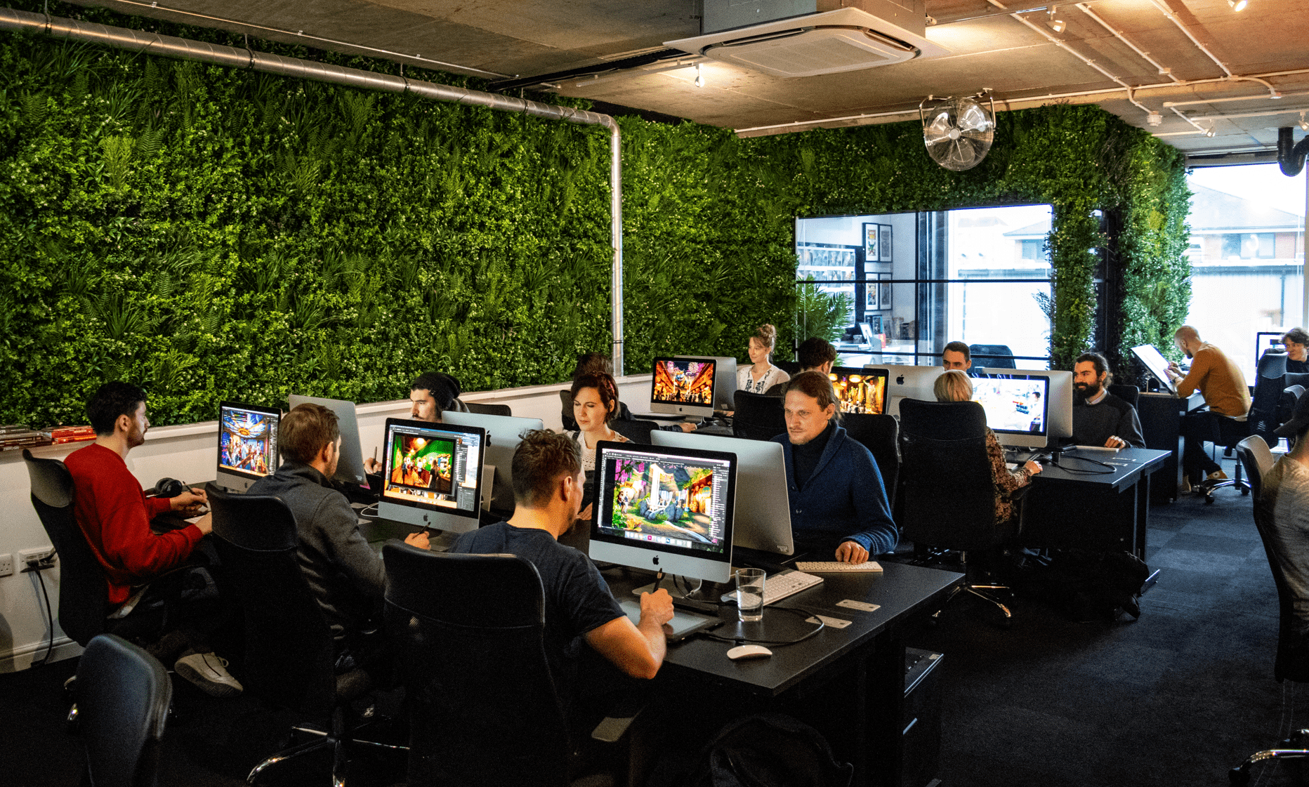 People in a office environment creating concept art next to a wall with grass on it