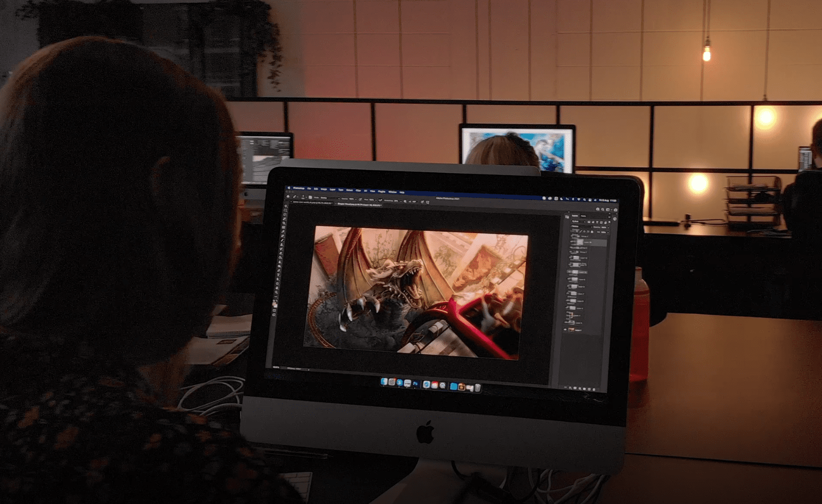 A person creating concept art on Photoshop on a computer in a dimly lit room