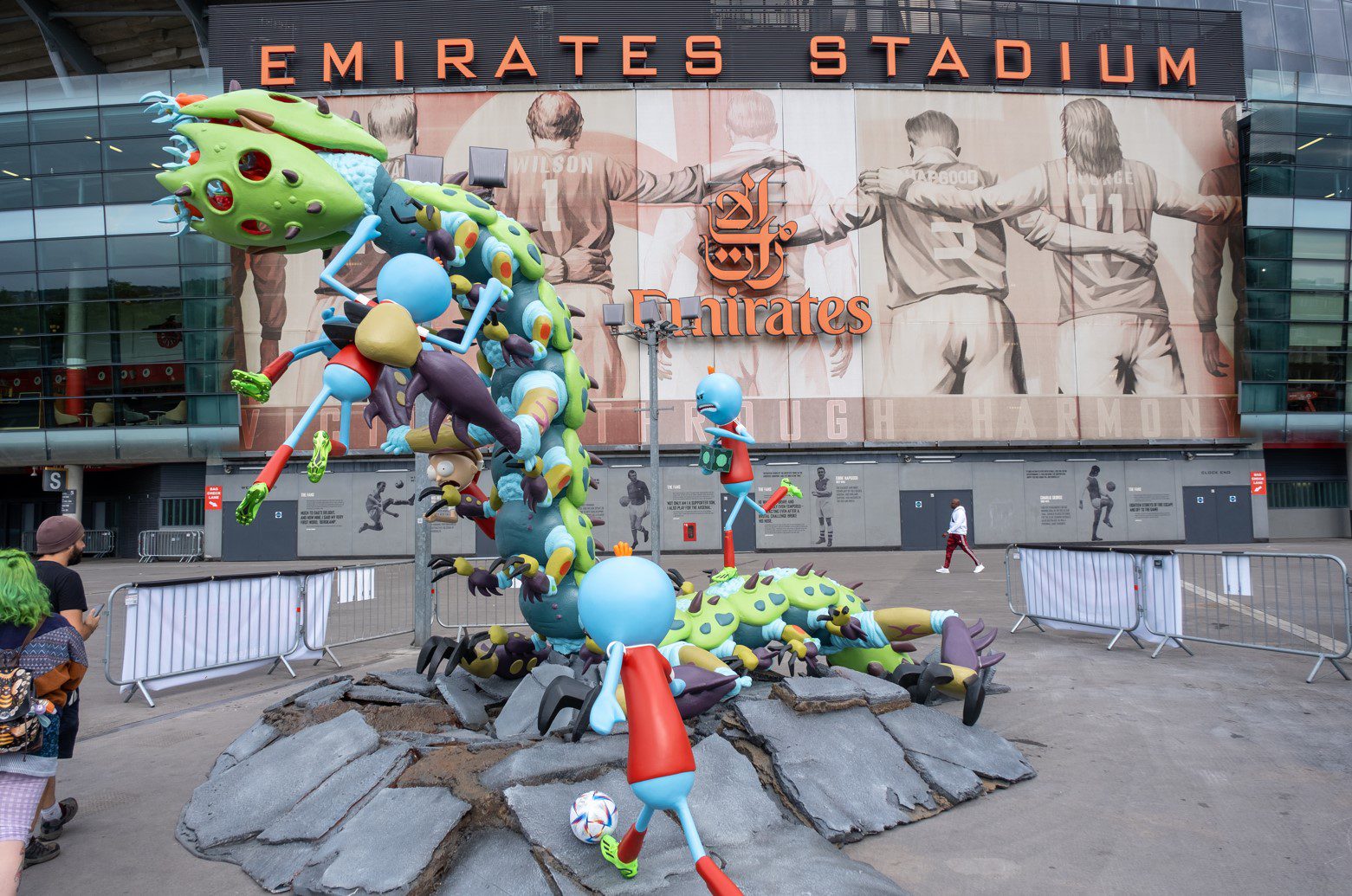 A blue and green monster emerging from the ground in front of emirates stadium